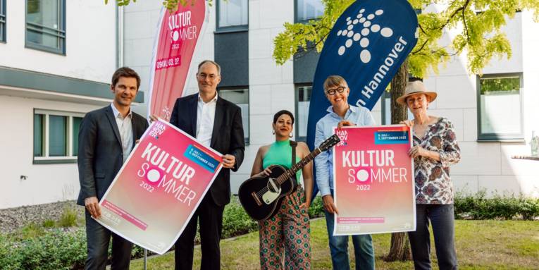Zwei Männer und drei Frauen stehen für ein Gruppenbild beieinander und zeigen Infos zum Kultursommer 2022 der Region Hannover in die Kamera.
